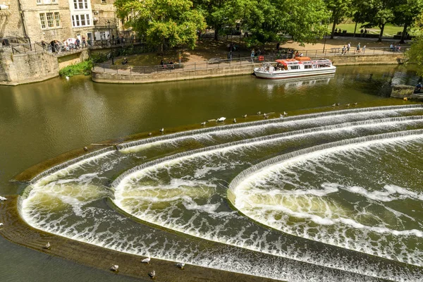 Bath, İngiltere - Temmuz 2019: Bath'ın merkezinde Avon Nehri üzerinde pulteney Weir şeklinde at nalı şeklinde. Bir turist teknesi arka planda.