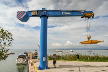 Bardolino, Garda Gölü, İtalya - Eylül 2018: Bardolino yakınlarındaki Garda Gölü'ndeki bir marinada uzaktan kumandalı vinç işleten işçi.