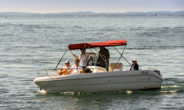 Garda Gölü, İtalya - Eylül 2018: Garda Gölü'ndeki Garda kasabasında limanın yanından yavaşça geçen küçük bir motorlu teknedeki insanlar.