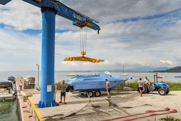 Bardolino, Garda Gölü, İtalya - Eylül 2018: Bardolino yakınlarındaki Garda Gölü'ndeki bir marinada bir tekneyi suya kaldırmak için uzaktan kumandalı vinç işleten işçi.