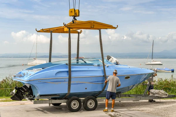 Bardolino, Garda Gölü, İtalya - Eylül 2018: Bardolino yakınlarındaki Garda Gölü'ndeki bir marinada tekneyi suya kaldırmaya çalışan işçi, kayışları kontrol ediyor.