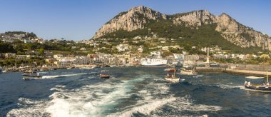 Isle Of Capri, İtalya - Ağustos 2019: Capri adasındaki limanın panoramik manzarası. Bir ferrry limana demirledi ve küçük tekneler limandan ayrılıyor..