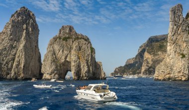 Isle Of Capri, İtalya - Ağustos 2019: Capri kıyılarında Faraglioni kaya oluşumu. Küçük tekneler kemerden geçiyor..