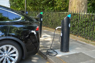 LONDON, ENGLAND - JULY 2018:  Care plugged into a charging point for electric cars kerb-side on a street in central London clipart