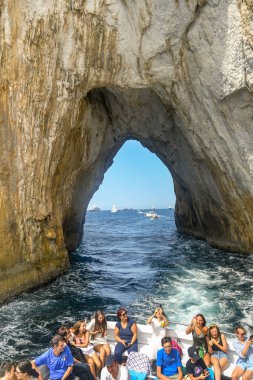 Isle Of Capri, İtalya - Ağustos 2019: Capri açıklarındafaraglioni kaya oluşumu kemer geçti bir teknenin arka insanlar.