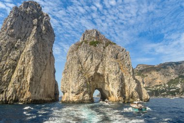 Isle Of Capri, İtalya - Ağustos 2019: Capri kıyılarında Faraglioni kaya oluşumu. Küçük tekneler kemerden geçiyor..
