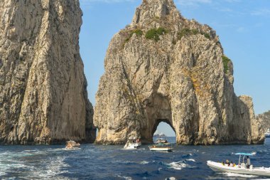 Isle Of Capri, İtalya - Ağustos 2019: Capri açıklarındaFaraglioni kaya oluşumunun kemerinden geçmek için kuyruğa giren küçük tekneler.