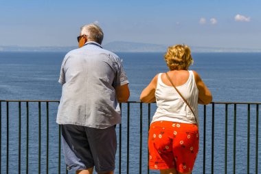 Sorrento, İtalya - Ağustos 2019: Sorrento'da kayalıkların üzerinde metal korkuluklara yaslanmış ve denize bakan erkek ve kadın