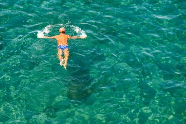 Sorrento, İtalya - Ağustos 2019: Sorrento'daki kayalıkların altındaki bir yüzme alanında denizde yüzen bir kişinin havadan görünümü