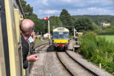 Gloucestershire, İngiltere - Eylül 2019: Gloucestershire ve Warwickshire Demiryolu'nda dizel çoklu ünite olarak görmek için trenin penceresinden dışarı yaslanan demiryolu meraklısı.