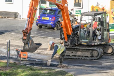 MOUNTAIN ASH, WOUTH WALES - Ekim 2018: Dağın Külleri 'nde yeni bir konut inşaatının kaldırımındaki boşluğu doldurmak için asfaltı düzleştiren inşaat işçisi.