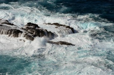 Dalgalar ve beyaz sprey denizdeki kayaların üzerine düşüyor.