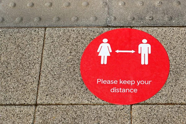 Yerde kırmızı bir etiket var. İnsanlardan sosyal mesafeyi korumalarını istiyor. İnsan yok. Boşluğu kopyala.