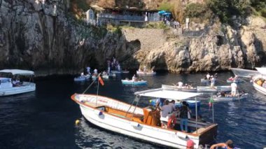 CAPRI, İtalya - Ağustos 2019: Küçük tekneler ve kayıklar yukarı aşağı sallanıyor ve turistleri Mavi Grotto 'ya götürüyorlar, Capri' deki bir deniz mağarasına. Soldan sağa dönüyor