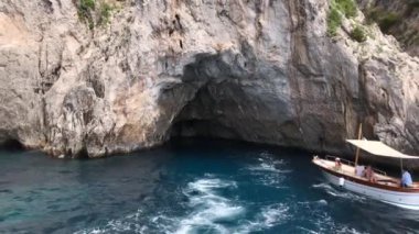 CAPRI, İtalya - Ağustos 2019: Capri kıyısındaki deniz mağaralarından birinden ayrılan teknenin uyanışı. Mağaraya başka bir tekne yaklaşıyor..