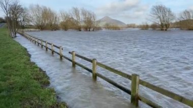 Ahşap çit ve tarlalar Severn Nehri 'nin aşırı hava koşullarında kıyılarını patlattıktan sonra çamurlu taşkın suyuyla sulanır.
