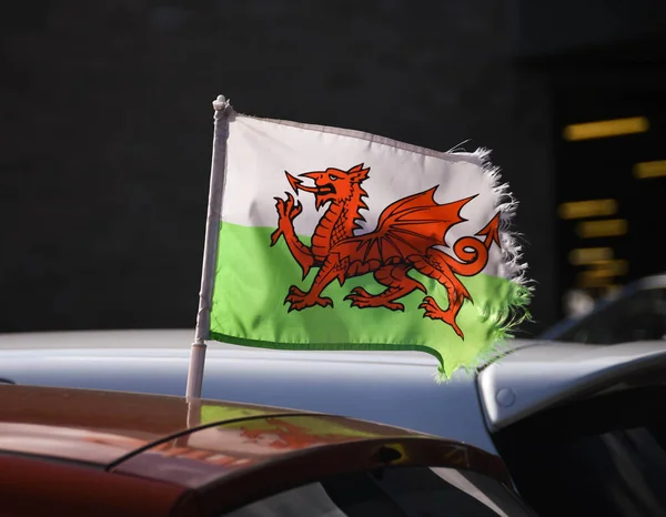 Small Welsh flag with a frayed edge back lit by sunlight against a dark background. No people.