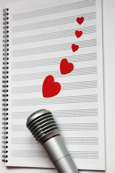 Microphone and paper red hearts are located on a clean music notebook. The concept of music and love. Valentines day