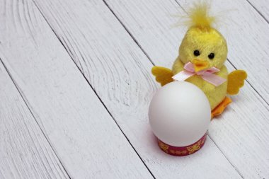 Beyaz tavuk yumurtası, komik sarı tüylü oyuncak tavuğun yanında bulunur. Paskalya tatili konsepti. Boş boşluk.