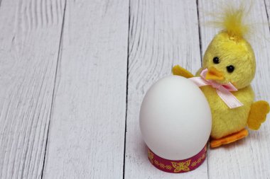 Beyaz tavuk yumurtası, komik sarı tüylü oyuncak tavuğun yanında bulunur. Paskalya tatili konsepti. Boş boşluk.