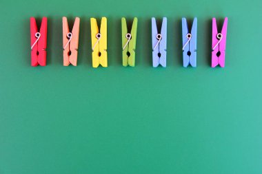 Ahşap clothespins gökkuşağı renkleri yeşil bir arka plan üzerinde üst üste düzenlenmiştir.