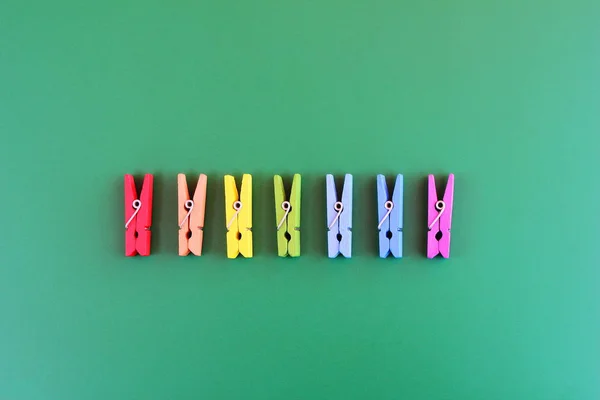 Wooden clothespins rainbow colors are arranged in a row on a green background.