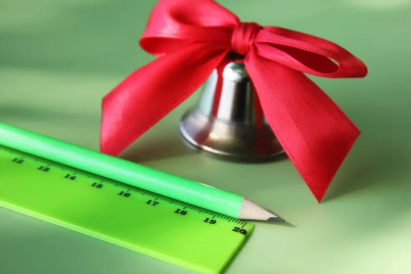 Regla Verde y un lápiz cerca de la campana con un lazo rojo. Regreso a la escuela . —  Fotos de Stock