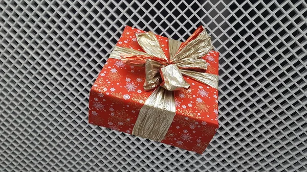Regalo de Navidad en un paquete brillante con un hermoso lazo en el fondo de la red con células pequeñas. El concepto de las vacaciones de año nuevo . —  Fotos de Stock