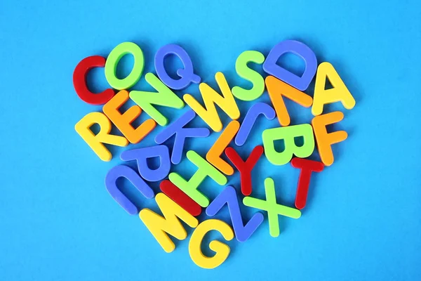 Multicolored letters of the English alphabet are laid out in the shape of a heart on a blue background.