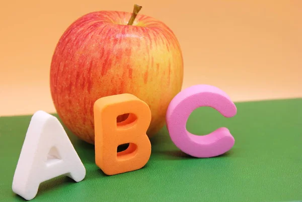 English ABC alphabet letters next to book and apple.