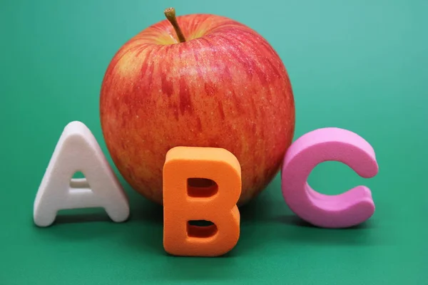English ABC alphabet letters next to book and apple.
