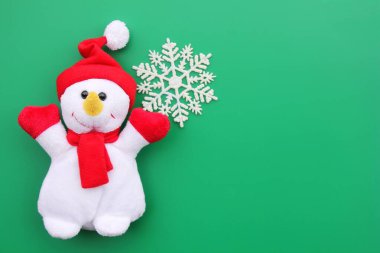 Yeşil bir arka plan üzerinde oyuncak gülümseyen kardan adam ve kar tanesi.