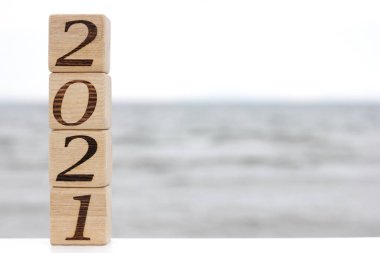 2021 numaralı ahşap bloklar, deniz kenarında bir piramit gibi birbirinin üstünde duruyor. Mutlu yıllar. Turizm, dinlenme ve seyahat kavramı.