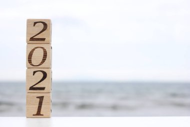 2021 numaralı ahşap bloklar, deniz kenarında bir piramit gibi birbirinin üstünde duruyor. Mutlu yıllar. Turizm, dinlenme ve seyahat kavramı.