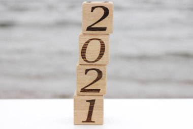 2021 numaralı ahşap bloklar, deniz kenarında bir piramit gibi birbirinin üstünde duruyor. Mutlu yıllar. Turizm, dinlenme ve seyahat kavramı.