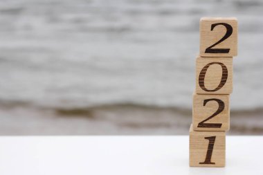 2021 numaralı ahşap bloklar, deniz kenarında bir piramit gibi birbirinin üstünde duruyor. Mutlu yıllar. Turizm, dinlenme ve seyahat kavramı.