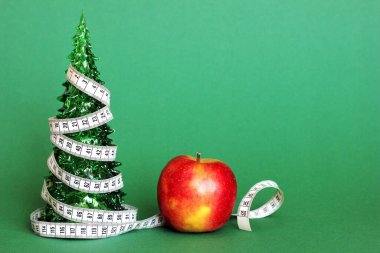 Bir santimetre uzunluğunda bir kurdele, Apple 'ın yanındaki küçük yeşil bir Noel ağacının etrafına sarılmış. Noel tatili boyunca sağlıklı ve sağlıklı yiyecek kavramı.