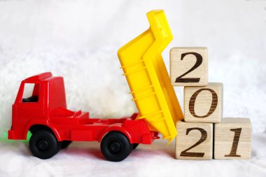 Beyaz arka planda oyuncak bir çöp kamyonu tarafından boşaltılan ahşap bloklarda 2021 yılının yeni yıl numarası. Mutlu yıllar..
