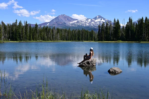 Mujer joven disfrutando de la vista de los volcanes Sisters reflejados en Scott Lake, Oregon . —  Fotos de Stock