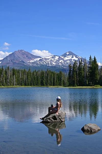 Mujer joven disfrutando de la vista de los volcanes Sisters reflejados en Scott Lake, Oregon . —  Fotos de Stock