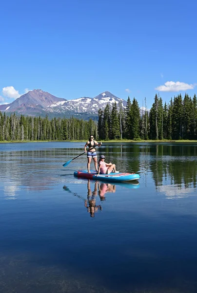 Dos mujeres jóvenes en el stand-up paddle board en Scott Lake, Oregon . — Foto de Stock