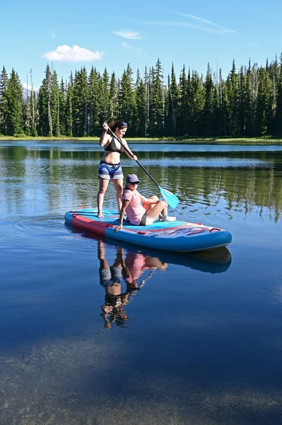 Dos mujeres jóvenes en el stand-up paddle board en Scott Lake, Oregon . — Foto de Stock