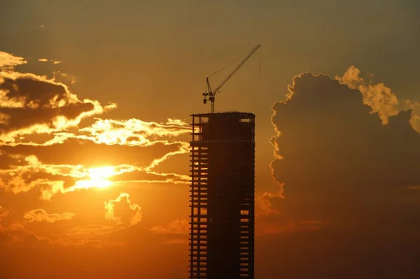 silhouette of a building with a crane on a background of clouds