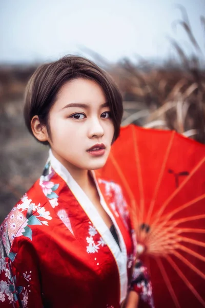 Beautiful Asian woman wearing traditional red kimono posing on field