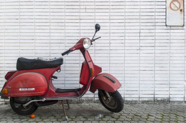 Eski Vespa gibi kırmızı motosiklet bir ızgara beyaz duvarın önünde park etmiş..