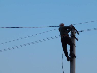 Elektrikçi direğin üzerinde özel kıyafetlerle çalışıyor