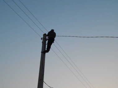 Elektrikçi direğin üzerinde özel kıyafetlerle çalışıyor