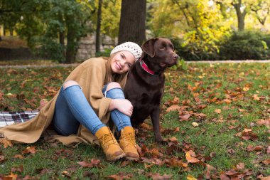 Güzel bir genç sarı saçlı kadın onun büyük kahverengi labrador köpek parkında sonbahar düşen yapraklar yığını ile eğleniyor