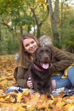 Güzel bir genç sarı saçlı kadın onun büyük kahverengi labrador köpek parkında sonbahar düşen yapraklar yığını ile döşeme