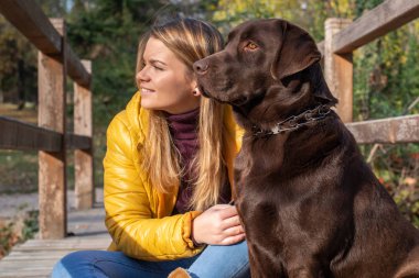 Güzel bir genç sarı saçlı kadın onun büyük kahverengi labrador köpek Park ile eğleniyor